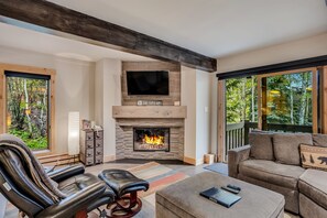 A cozy living room with a fireplace, leather seating, and large windows offering a view of the outdoors.