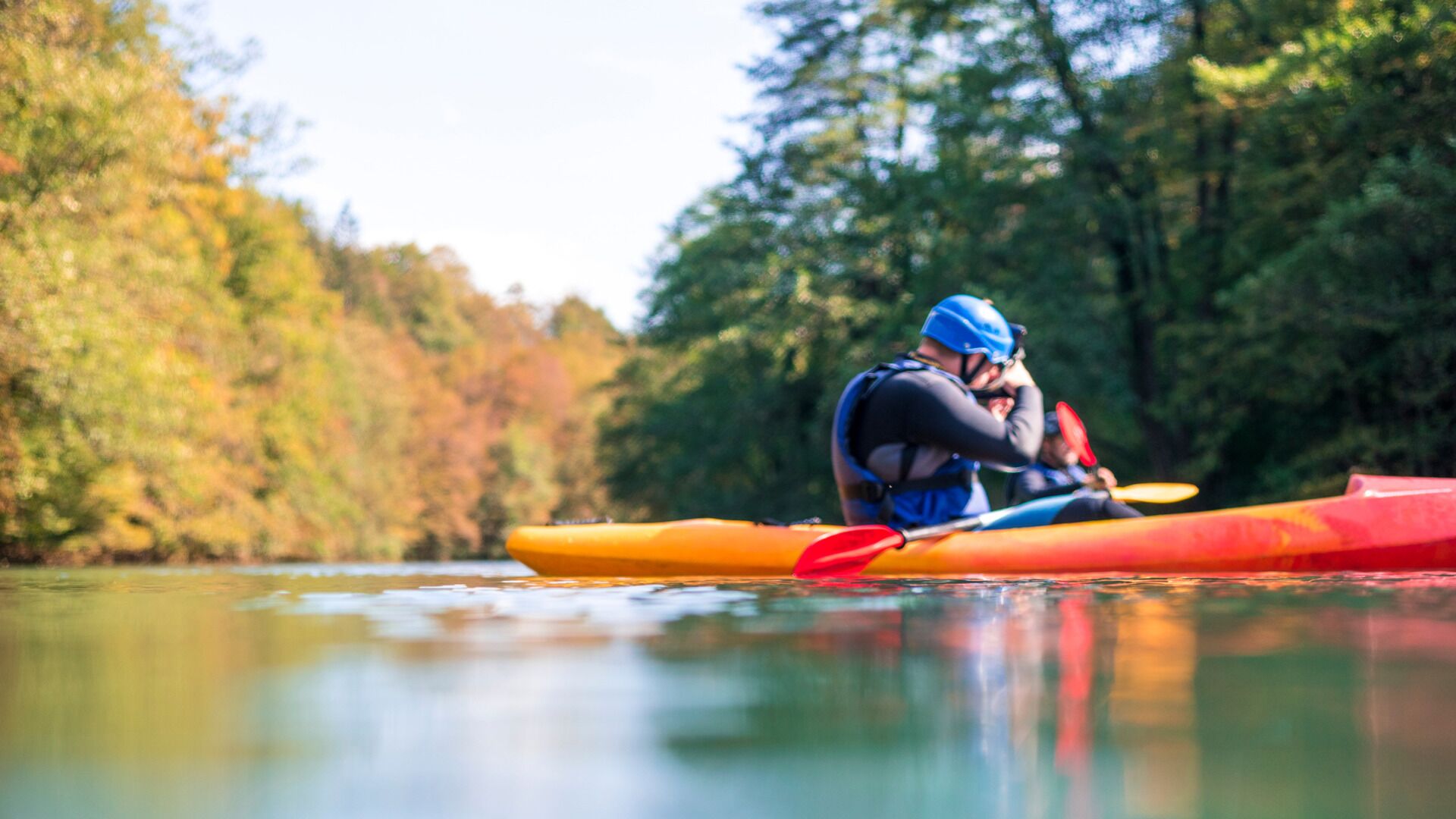 Una persona practica kayak en un río tranquilo rodeado de árboles.