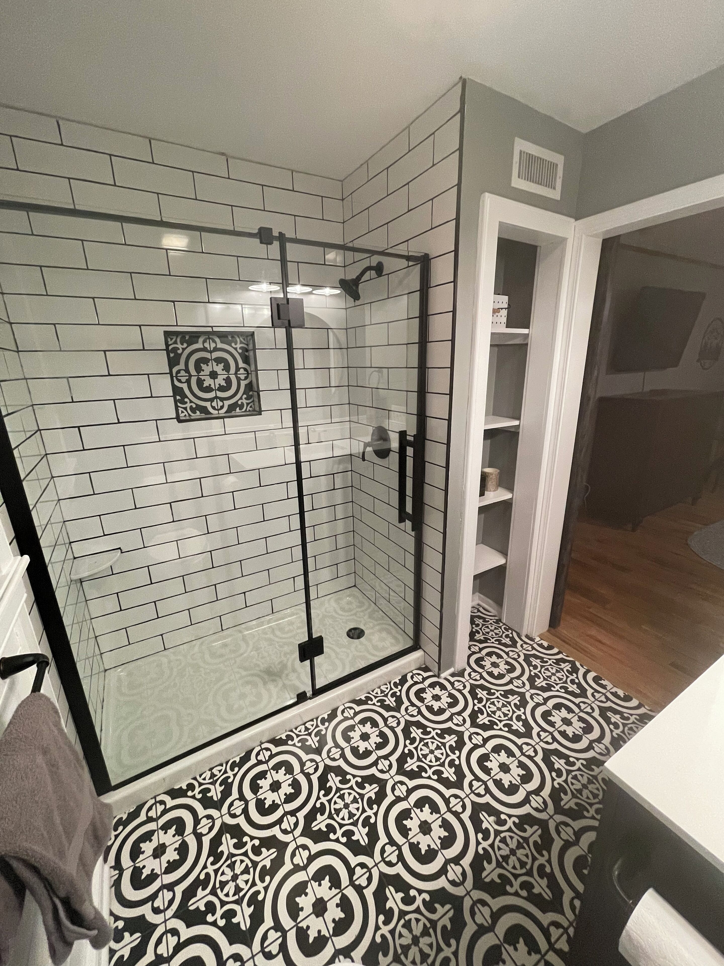 A bathroom with a glass-enclosed shower, white tiled walls, and patterned floor tiles.