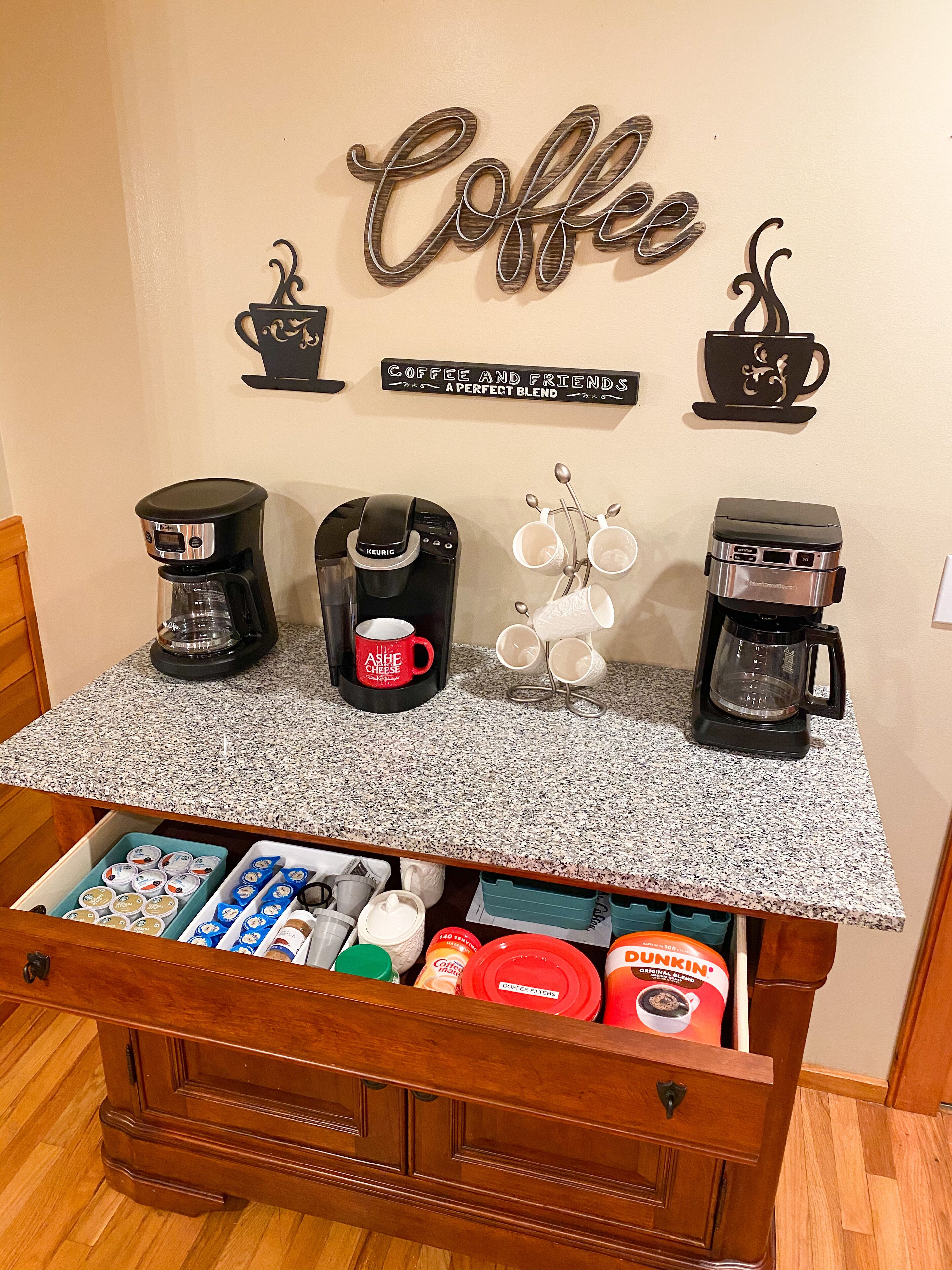 Un comptoir de cuisine avec trois machines à café, une tasse à café et une décoration murale sur le thème du café.