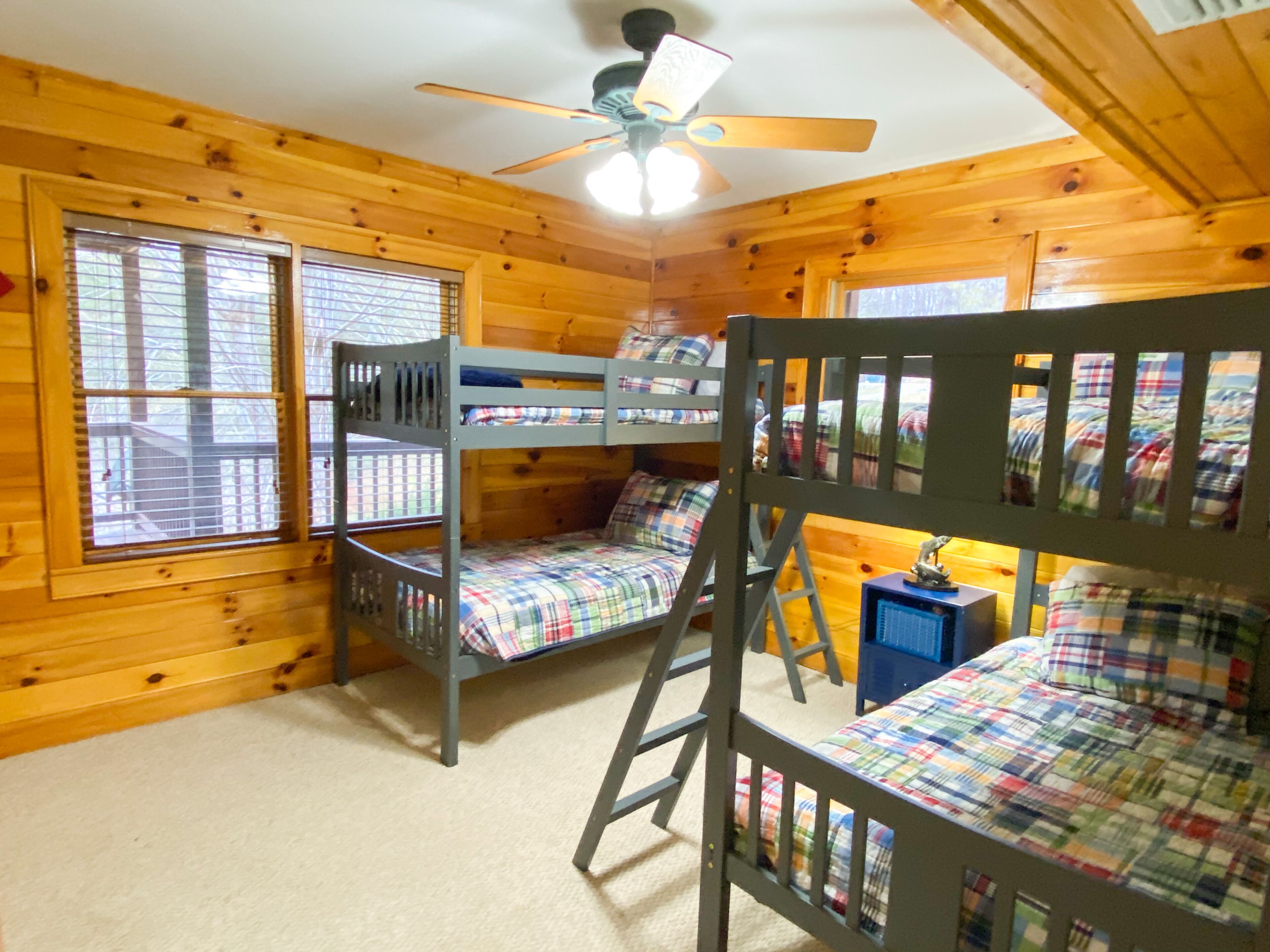 A cabin with wooden walls, a ceiling fan, bunk beds, and windows.