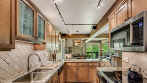 A kitchen with wooden cabinets, a granite countertop, a built-in oven, and a large window overlooking a green landscape. - 🏔️Ski-In, Ski-Out Condo~Hot Tub~Interlude 205🏔️ (Snowmass Village)