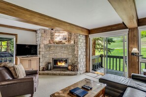 A cozy living room with a stone fireplace, leather furniture, and a large window overlooking a deck.