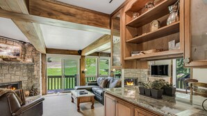 A cozy living area with a stone fireplace, leather sofa, and a large window overlooking a garden. - 🏔️Ski-In, Ski-Out Condo~Hot Tub~Interlude 205🏔️ (Snowmass Village)