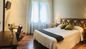 A hotel room with a bed, bedside table, lamp, and a desk with a chair and a vase of flowers. - Oca Aldeaduero Hotel (Saucelle)