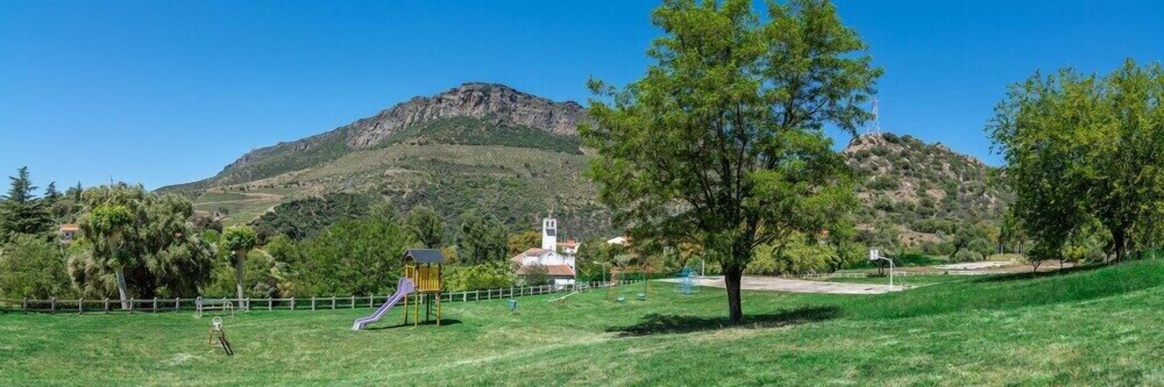 A grassy field with a playground, a church, and a mountain in the background.