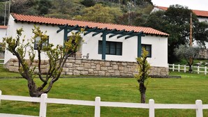 A white building with a red-tiled roof, stone foundation, and a white picket fence in the foreground. - Oca Aldeaduero Hotel (Saucelle)