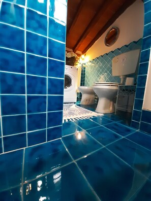 Un baño con azulejos azules, lavadora, dos inodoros y un tapete estampado.