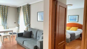 A room with a grey sofa, a wooden door, a bed with yellow pillows, and a framed picture on the wall. - Pena Santa Hotel (Onis)