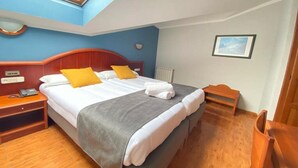 A hotel room with a bed, a bedside table, a nightstand, a chair, a small table, a picture on the wall, and a skylight. - Pena Santa Hotel (Onis)