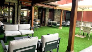 An outdoor patio area with artificial grass, green and white outdoor furniture, and a stone building entrance. - Pena Santa Hotel (Onis)