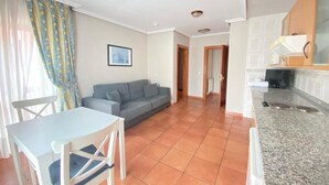 A living room with a grey sofa, a dining table with chairs, and a kitchen area with a granite countertop and cabinets. - Pena Santa Hotel (Onis)