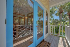 A wooden deck with a white railing, a blue door, and a view of palm trees. - Wake up on the waters of Tampa Bay in a north Anna Maria home. (Anna Maria)