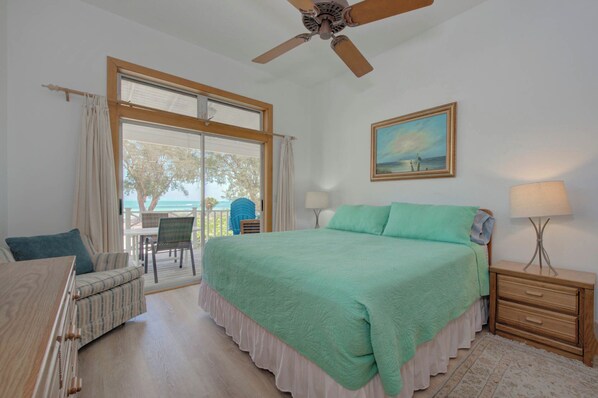 A bedroom with a large bed, a ceiling fan, a painting, and a view of the ocean through a sliding door. - Wake up on the waters of Tampa Bay in a north Anna Maria home. (Anna Maria)
