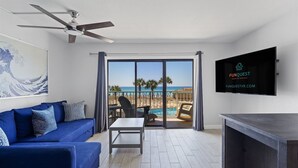 Une chambre moderne avec un canapé bleu, une petite table, un ventilateur de plafond et un écran de télévision affichant le logo « FUNQUEST Vacation Rentals ».