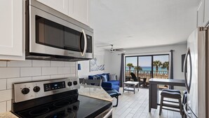 Une cuisine moderne équipée d’un four à micro-ondes et d’une cuisinière intégrés, un coin repas avec une table et des chaises, et un balcon avec vue sur la plage.