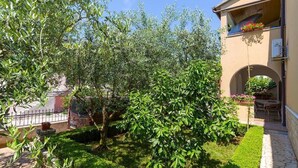 Une cour avec une pelouse bien entretenue, un arbre et un bâtiment doté d’une entrée en arc de cercle.