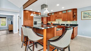 A modern kitchen with wooden cabinets, a stainless steel refrigerator, and a bar area with two stools.