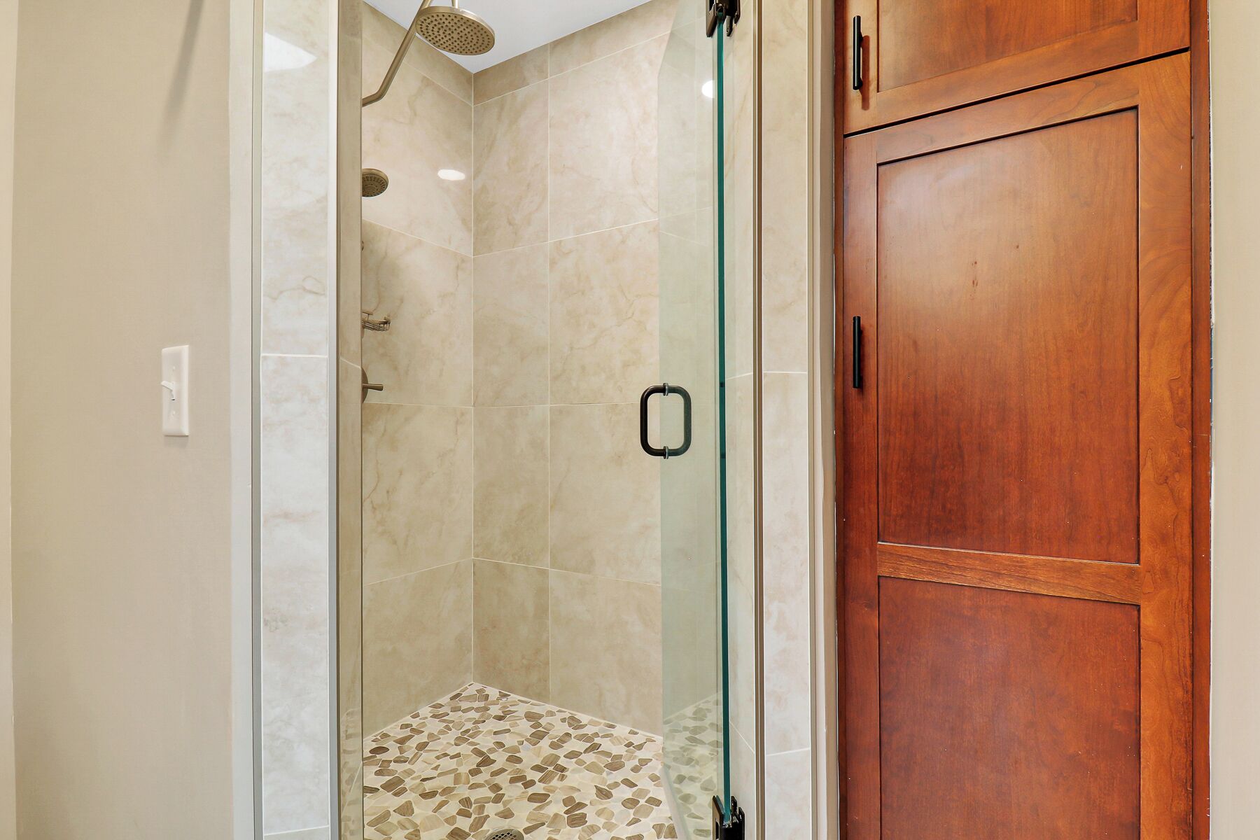 Een douche met een glazen deur, een houten kast en een betegelde vloer.