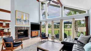 A spacious living room with a fireplace, a television, and a large window overlooking a golf course.
