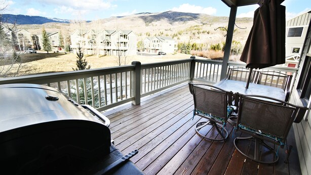 A wooden deck with a grill, a table with chairs, and a view of a mountainous landscape. - Big Unit, Deck! Walk to Rec Trail, Fishing. Easy Drive to Dining, Events (Silverthorne)
