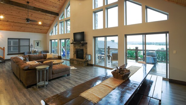 Un salón amplio con techo de madera, ventanas grandes, chimenea y vistas al exterior.