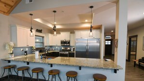 Una cocina moderna con encimeras de granito, electrodomésticos de acero inoxidable y taburetes de bar.