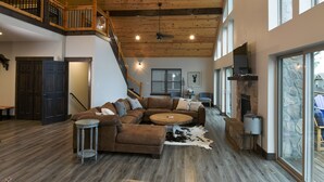 Un salón amplio con techo de madera, un sofá modular grande, una mesa de centro redonda y una chimenea de piedra.
