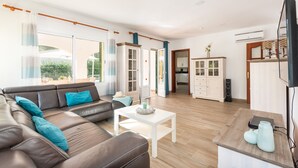 A spacious living room with a brown leather sofa, a white coffee table, and a kitchen area with cabinets and a television.