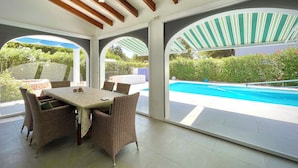 A covered outdoor dining area with wicker furniture and a view of a swimming pool.