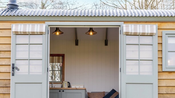Un chalet confortable, avec une façade en bois, un petit coin cuisine et un espace salon comprenant un canapé et des coussins.