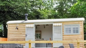 Une petite cabane en bois, dont la porte est ouverte, laissant entrevoir une pièce avec une fenêtre et une chaise à l’intérieur.