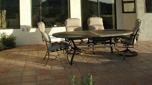 Een terras buiten met een ronde tafel en vier stoelen, grote ramen en een vloer van stenen tegels.