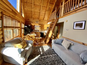 A log cabin interior with a dining area, a sofa, and a staircase.