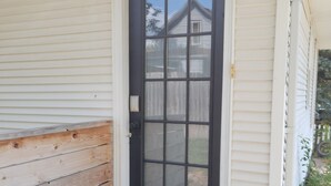 Una puerta principal con un panel de vidrio negro, un escalón que la precede y un banco de madera a la izquierda.
