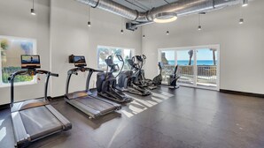 A gym with treadmills, ellipticals, and a rowing machine. There are large windows with a view of palm trees and the ocean. - Escapes to the Shores 1702 by Liquid Life (Orange Beach)