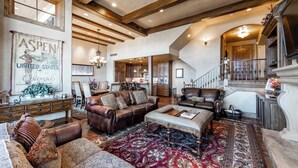 A spacious living room with a large rug, leather sofas, and a wooden ceiling.