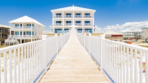 A wooden boardwalk leading to a large white building with multiple balconies and windows, surrounded by beachside properties. - Seaside East and West ( 2 Properties - 24 Bedrooms) (Gulf Shores)