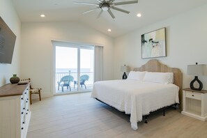 Une chambre avec un grand lit, un ventilateur de plafond, une table de chevet avec une lampe, une chaise et un balcon avec vue.