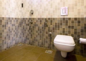 A bathroom with a toilet, a shower, and a tiled wall.