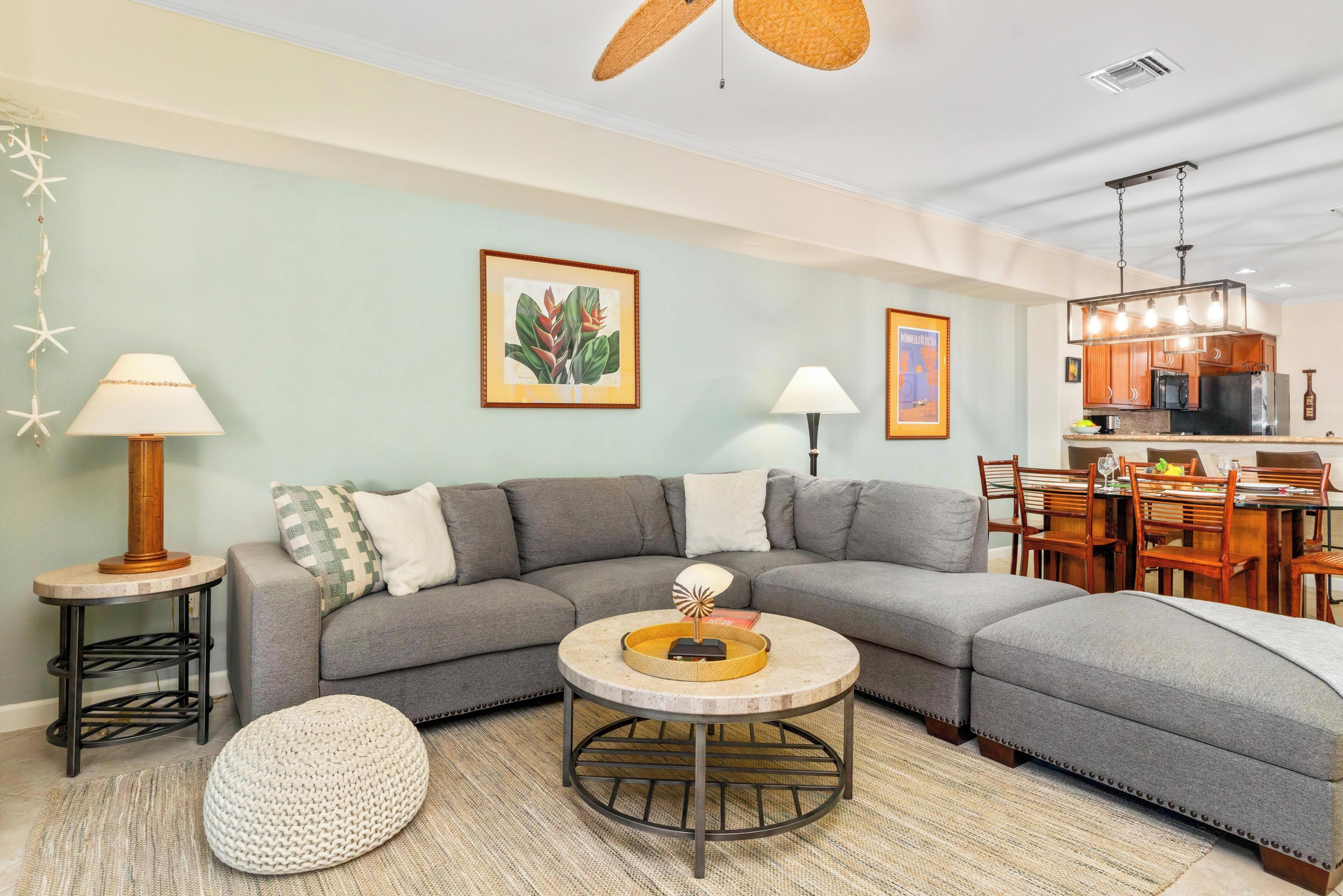 A modern living room with a gray sectional sofa, a round coffee table, a small side table, and a dining area with wooden chairs and a table.