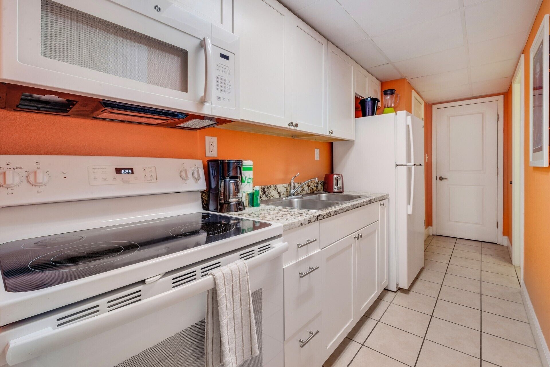 A compact kitchen with white cabinets, a microwave, a stove, and a sink.
