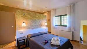 A hotel room with a brick wall, a bed with a dark bedspread, two bedside lamps, a window with curtains, and a radiator. - Alegría de Ronda by Ruralidays (Málaga)