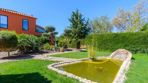 A garden with a pond, a red building, and various plants. - Alegría de Ronda by Ruralidays (Málaga)