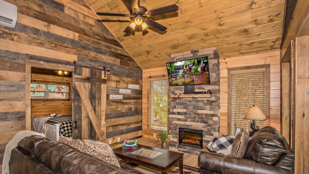 L’intérieur d’un chalet confortable, avec une cheminée, des canapés en cuir, un téléviseur et un ventilateur de plafond.