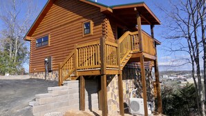 Une cabane en rondins dotée d’une terrasse en bois et d’un escalier menant à un balcon.