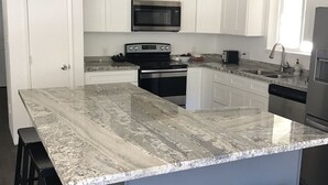 A kitchen with white cabinets, a granite countertop, a microwave, a stove, and a refrigerator. There are three black stools at the island. - NORTH LAKE TAHOE VACATION RENTAL WITH SKI AND MOUNTAIN VIEWS, HIKE & BIKE TRAILS (Incline Village)