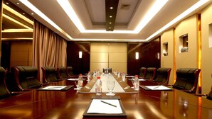 A conference room with a long table, multiple chairs, water bottles, and glasses. - Kingdom Narada Grand Hotel Yiwu (Jinhua)