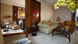 A well-lit living room with a sofa, armchairs, a coffee table, and a side table. There is a decorative vase with red branches on the side table. - Kingdom Narada Grand Hotel Yiwu (Jinhua)