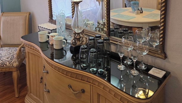A room with a large ornate mirror, a dresser with glassware, and a chair. - Charming Fruitland Park Getaway (Fruitland Park)